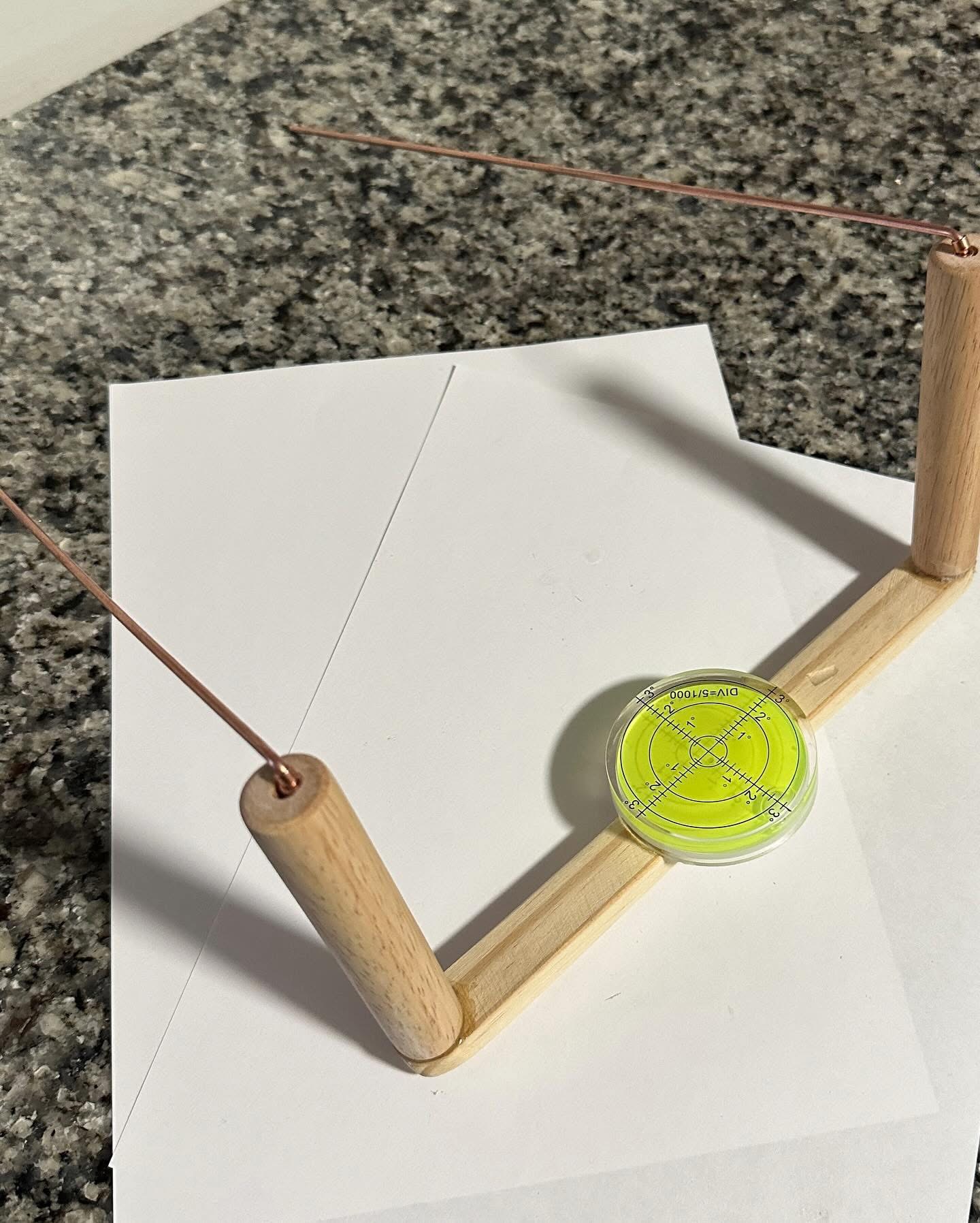 Modified dowsing rods locked together on a wooden bar with a central bubble level